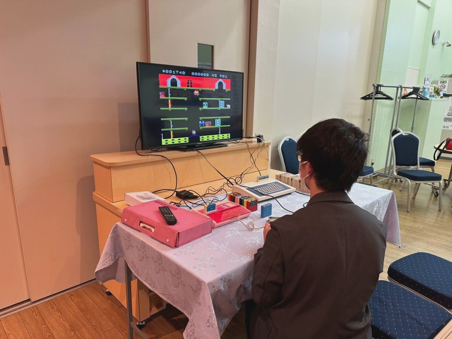 テーブルに置いた昔のゲーム機とカセットをつなぎ、モニターに映したゲームを男性が遊んでいる様子